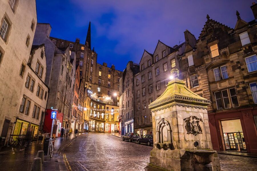Lamplit shopfronts on the Grassmarket below the Old Town at dusk